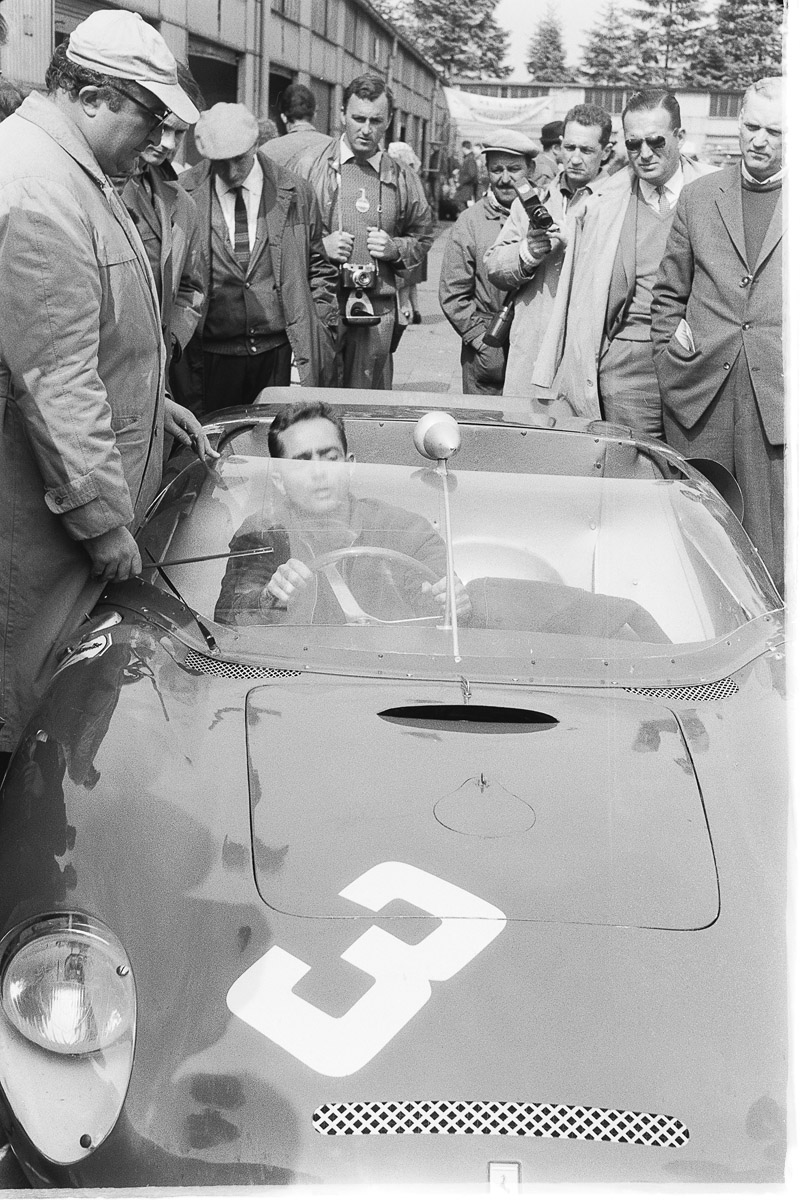 Phil Hill in seinem Ferrari mit vielen Männern um den Wagen herum
